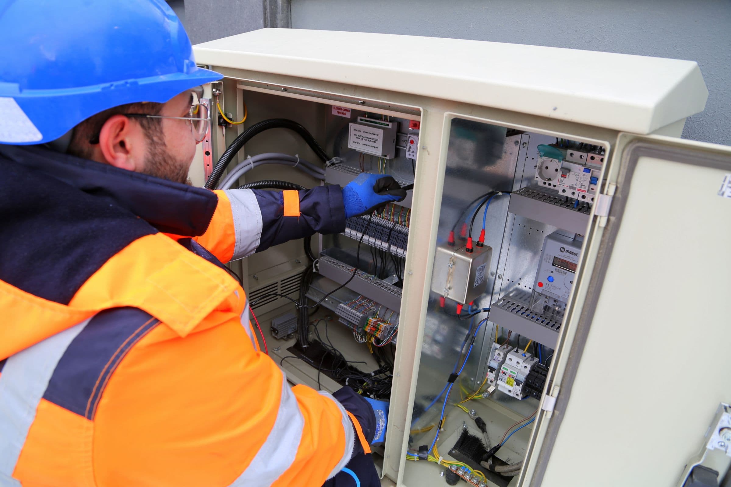 Technician in a hard hat and hi-vis working on the wiring inside an outdoor control cabinet